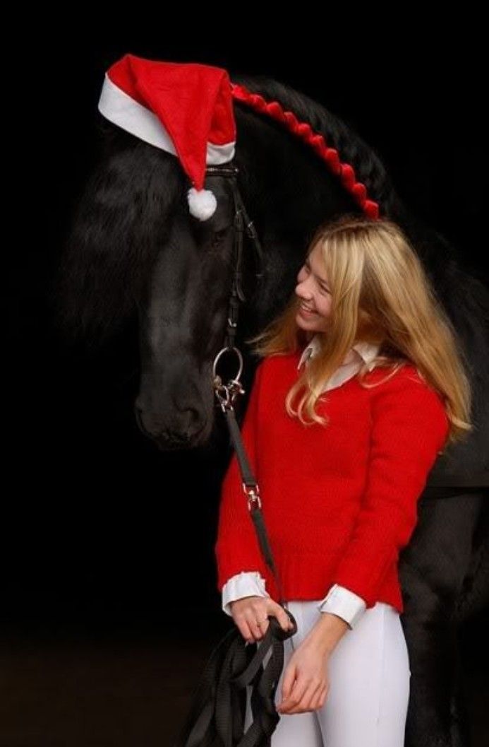 a woman in red sweater standing next to a black horse with santa hat on it's head