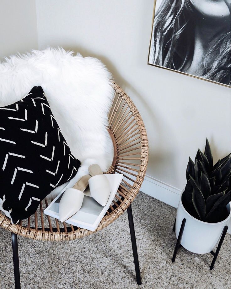 a wicker chair with black and white pillows on it next to a potted plant