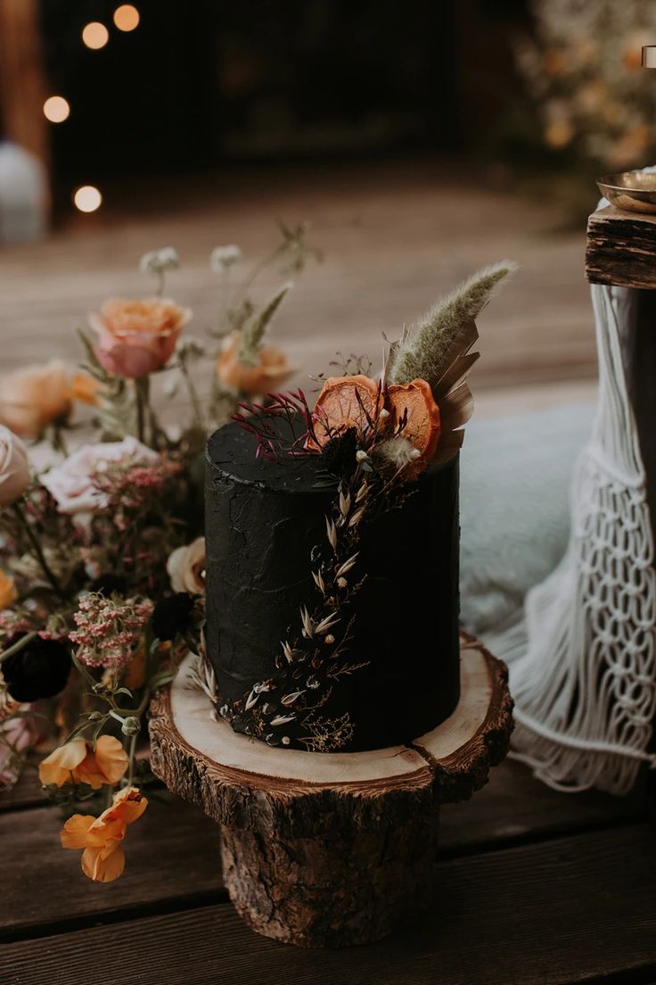 a black wedding cake with flowers and feathers on the top sitting on a wooden table