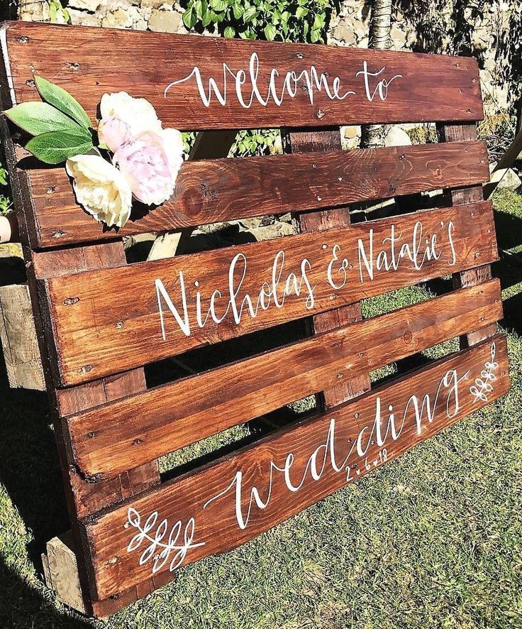 a wooden sign that says welcome to nicholas and nathan with flowers on it sitting in the grass