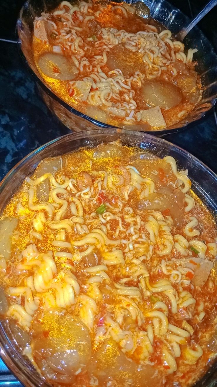 two pans filled with noodles and meat on top of a stovetop burner