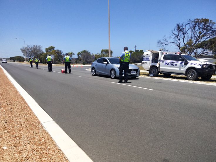 two police officers standing on the side of a road next to cars and an ambulance