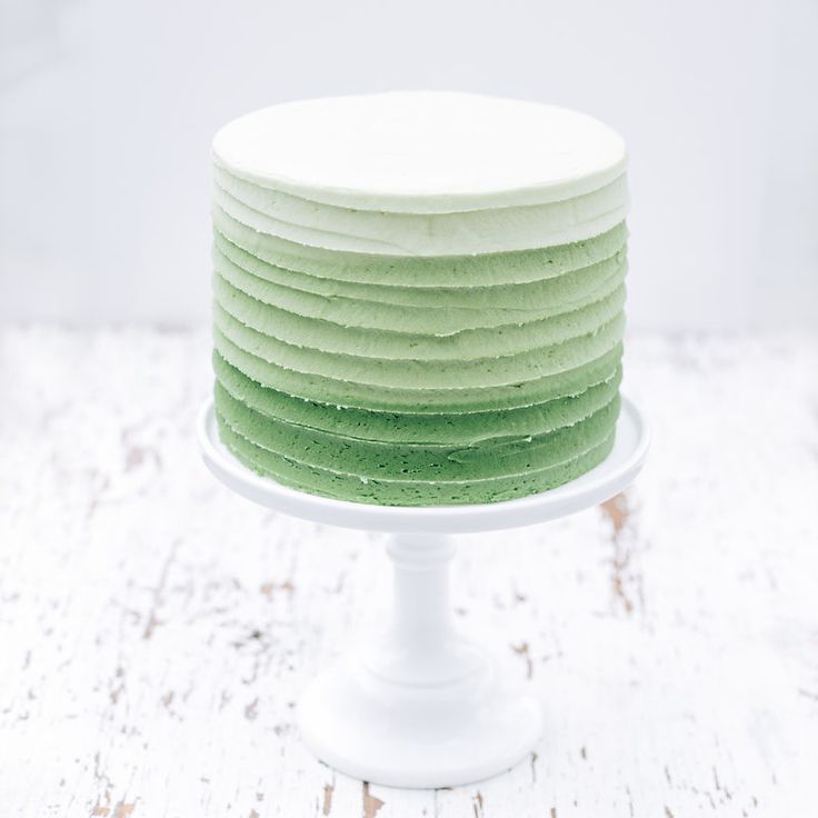 a white cake with green frosting sitting on top of a wooden table in front of a white wall