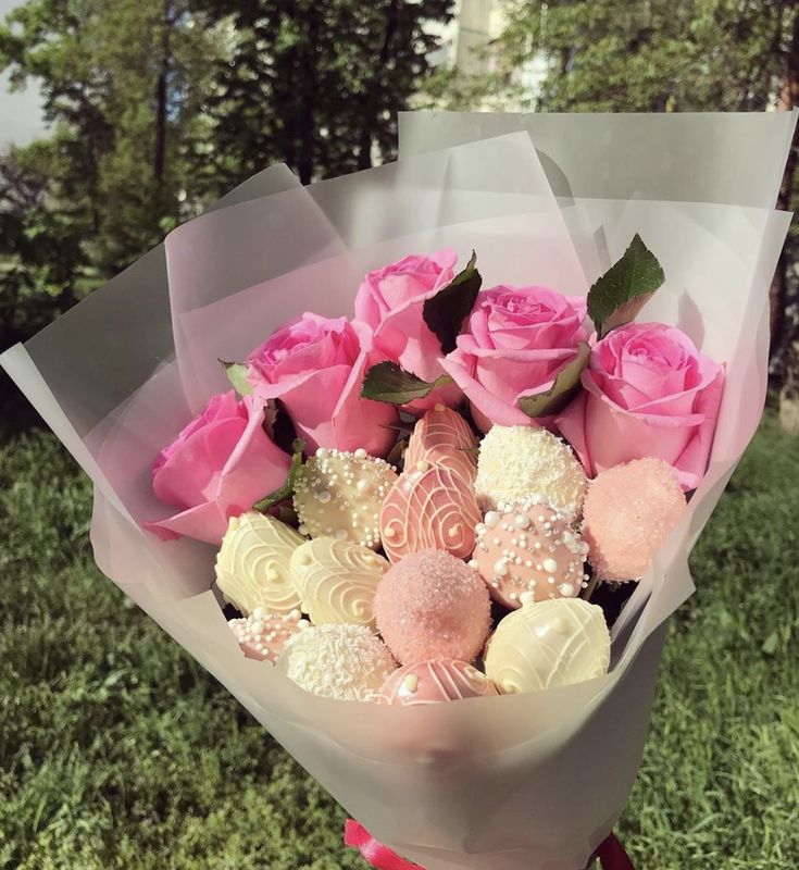 a bouquet of pink roses and white chocolates in a wrapper on the grass