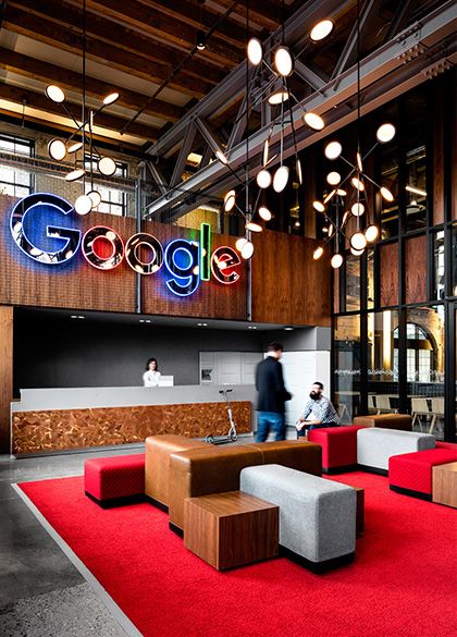 an office lobby with red carpet and lights hanging from the ceiling, two people walking by