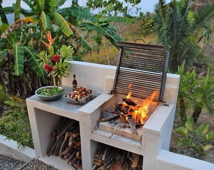 an outdoor bbq grill with fire and food on the outside, surrounded by tropical vegetation