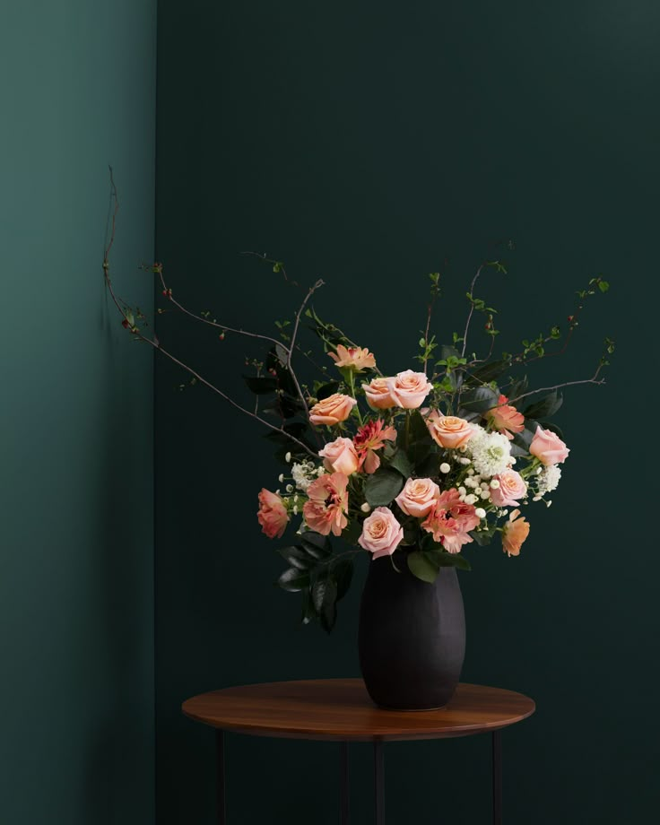 a black vase filled with pink and white flowers on top of a small wooden table