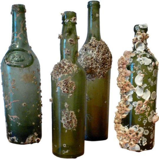 four green bottles with flowers on them are lined up against a white background and one is empty