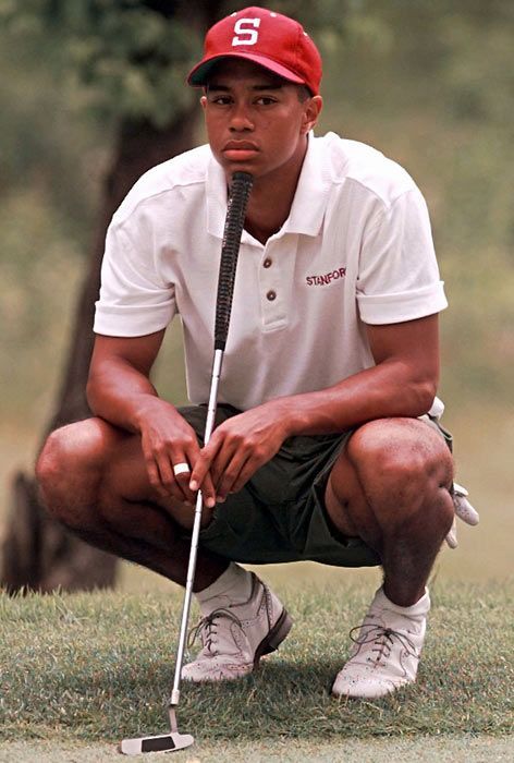 a man kneeling down with a golf club in his hand and wearing a red hat