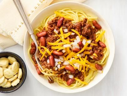 a white bowl filled with spaghetti and beans next to a small bowl of cashews