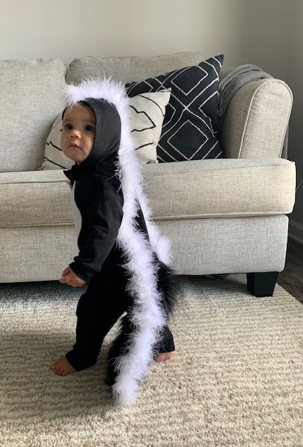 a toddler in a costume standing on the floor next to a couch and looking at the camera