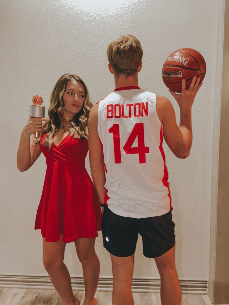 a man and woman in red dresses holding up a basketball while standing next to each other