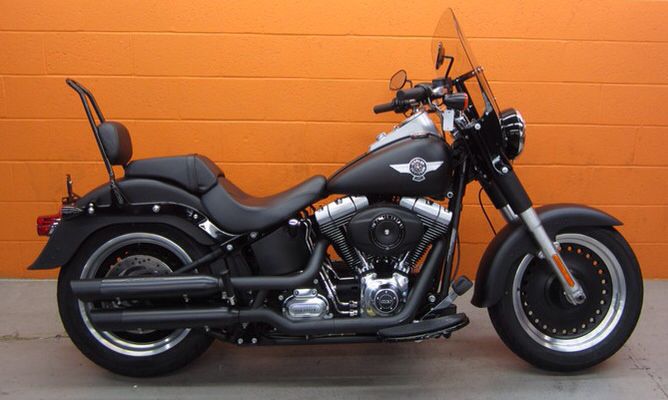 a black motorcycle parked in front of a orange wall with no one on the bike