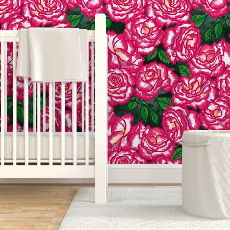 a white crib in front of a wall with pink roses on it