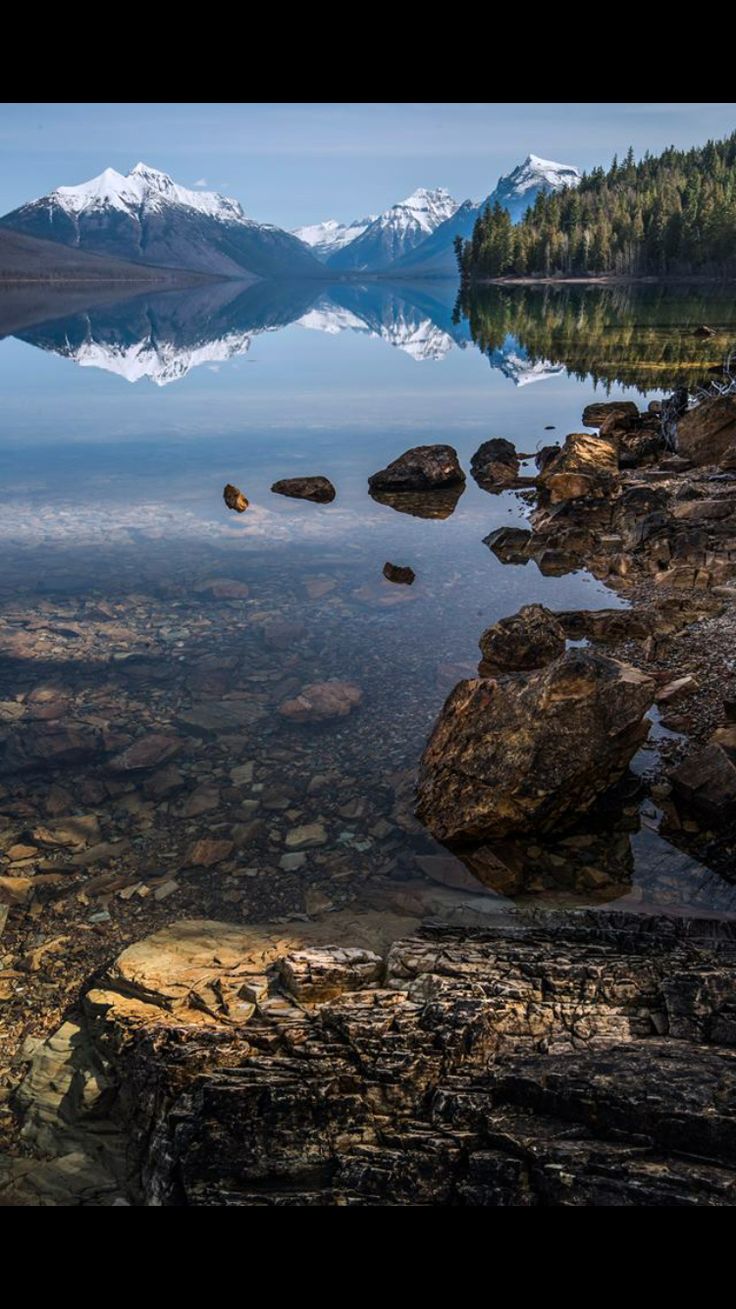 the mountains are reflected in the still water on the lake's shore, with rocks and boulders scattered around them