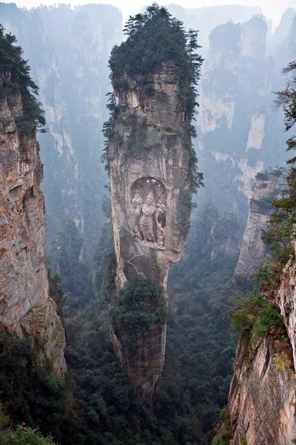 the mountains are covered in trees and rock formations, with faces carved into them on each side