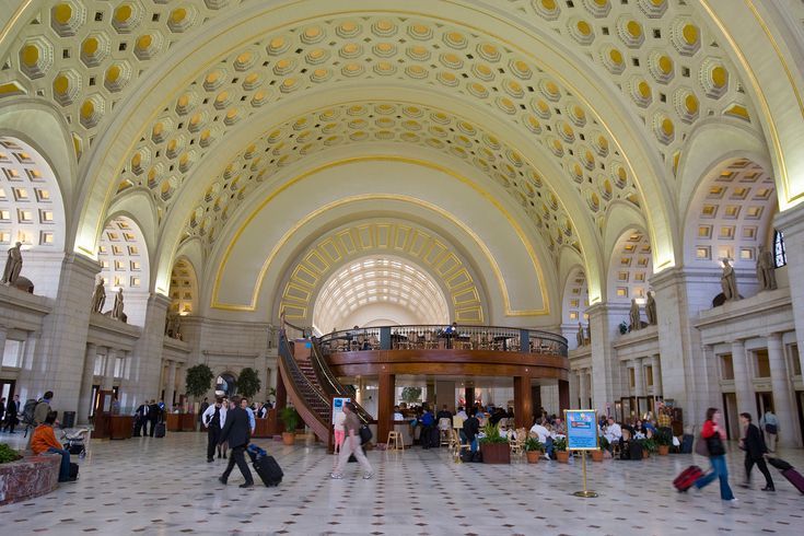 people are walking around in the lobby of a large building with high ceilings and arches