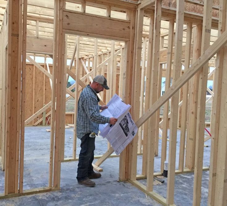 a man standing in the middle of a room with wood framing on it and looking at plans