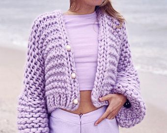 a woman standing on top of a beach next to the ocean wearing a purple sweater