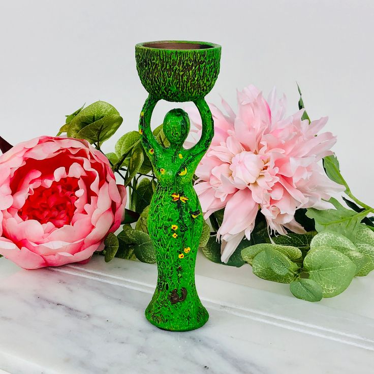 two green vases sitting on top of a white table next to pink flowers and greenery