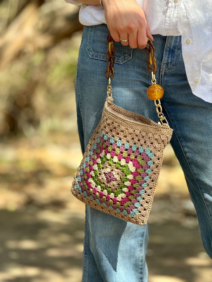 a woman is holding a crocheted purse in her left hand and wearing blue jeans