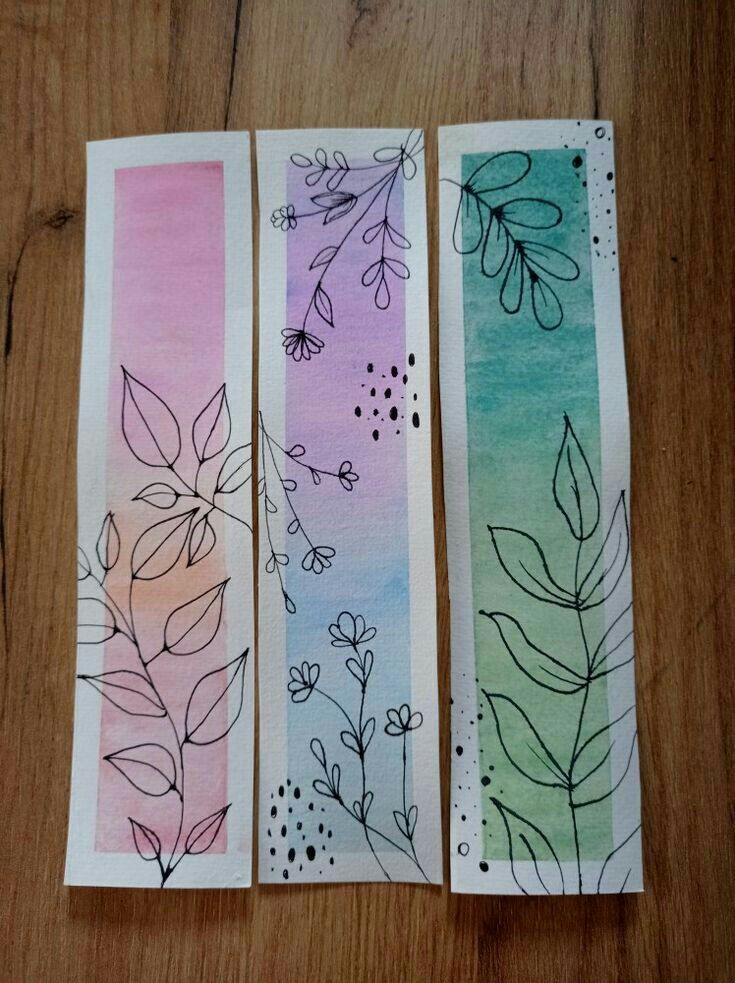 three bookmarks with flowers and leaves painted on them sitting on a wooden table next to each other