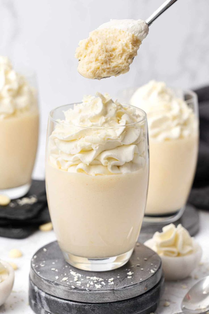 a spoon full of whipped cream on top of a glass cup with another bowl in the background