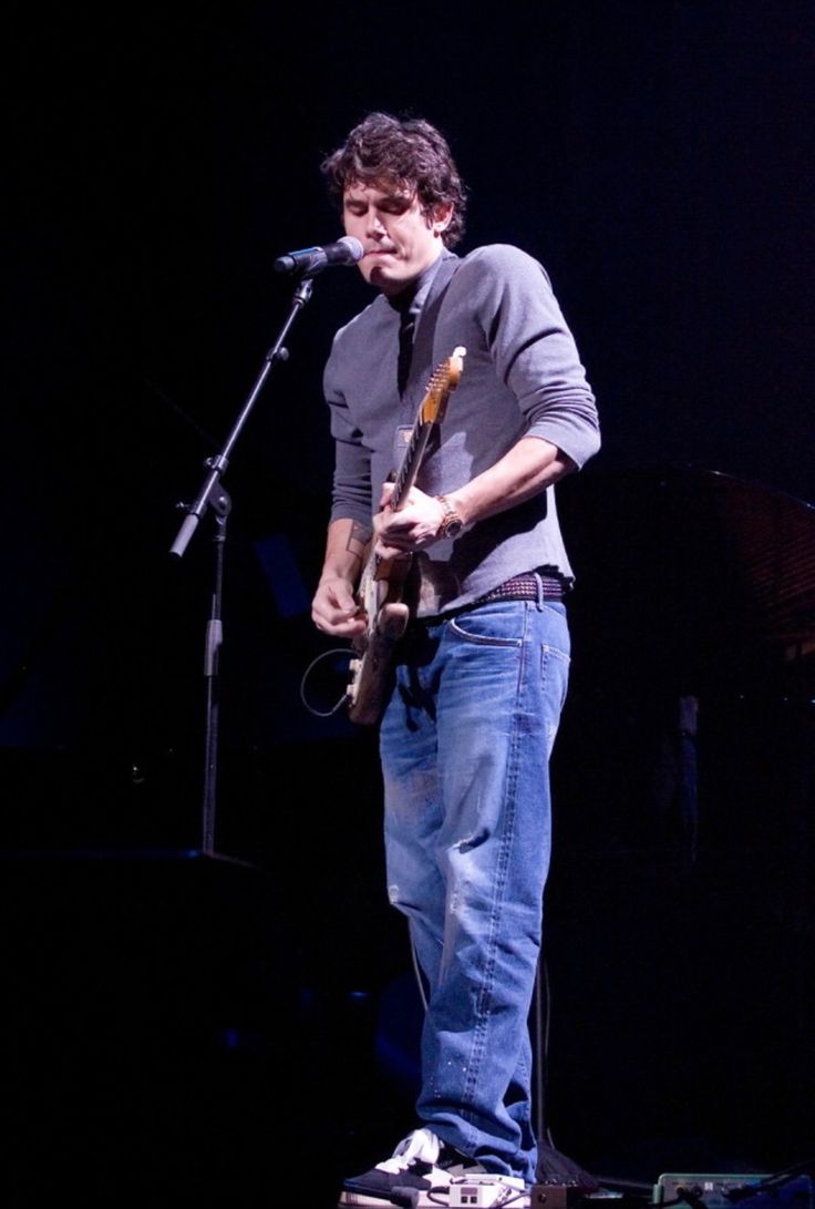 a man standing in front of a microphone while holding a guitar