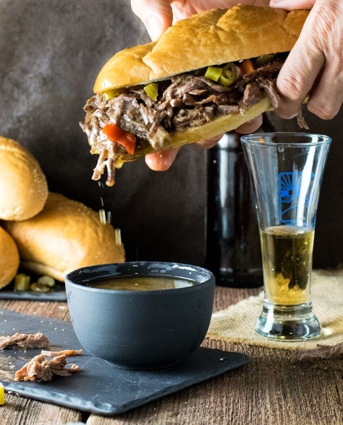 a person is holding a sandwich over a bowl of soup and a glass of beer