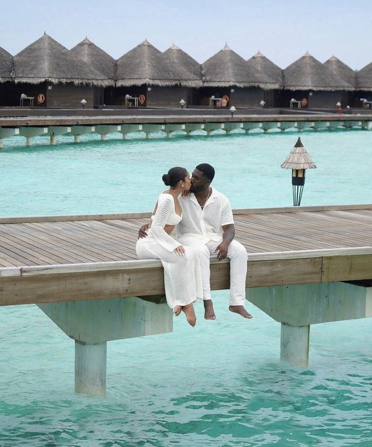 two people are sitting on a dock in the water and one person is kissing the other