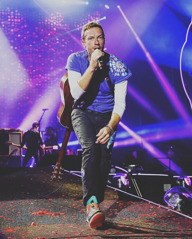 a man on stage singing into a microphone with lights in the back ground behind him