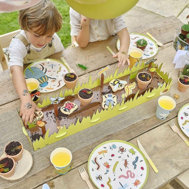 two children sitting at a picnic table with plates and cupcakes in front of them