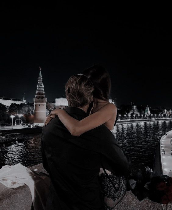 a man and woman sitting next to each other in front of a body of water