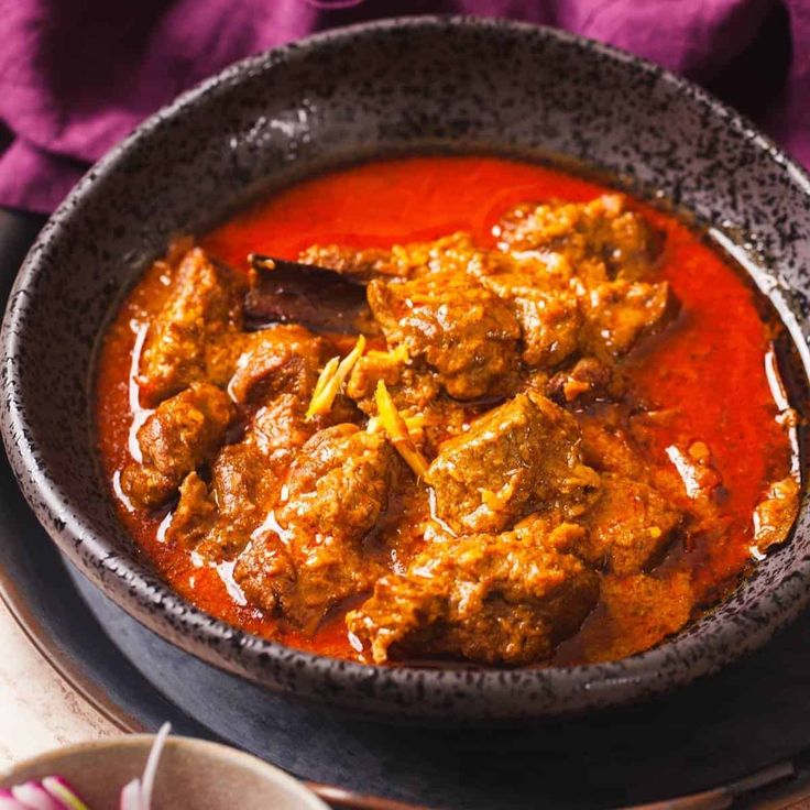 a bowl filled with meat and sauce on top of a wooden table next to silverware