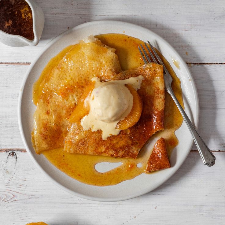 a white plate topped with french toast covered in syrup and ice cream next to orange slices