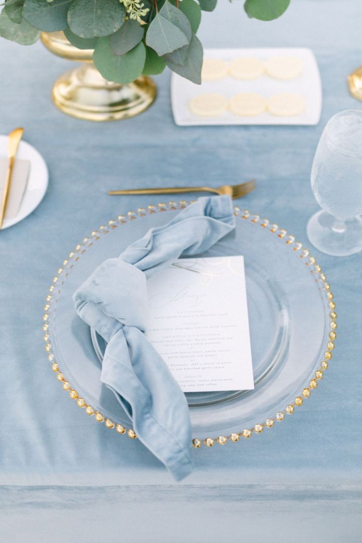 a table set with blue linens and gold place settings