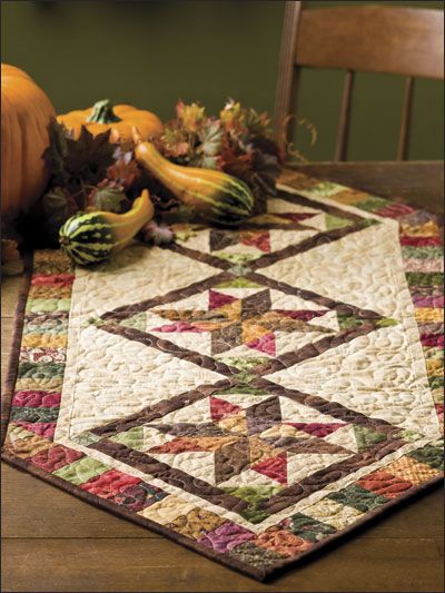 a quilted table runner with pumpkins and gourds on the table in the background