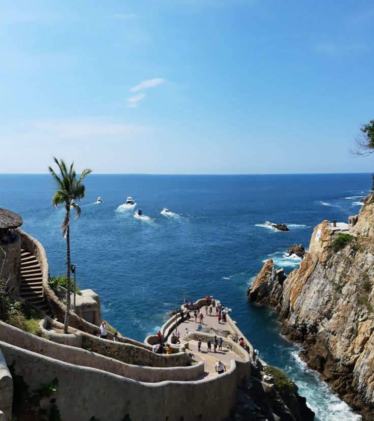 people are walking down the stairs to an ocean side area with boats in the water