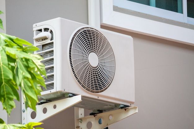 an air conditioner mounted on the side of a building next to a plant in front of a window