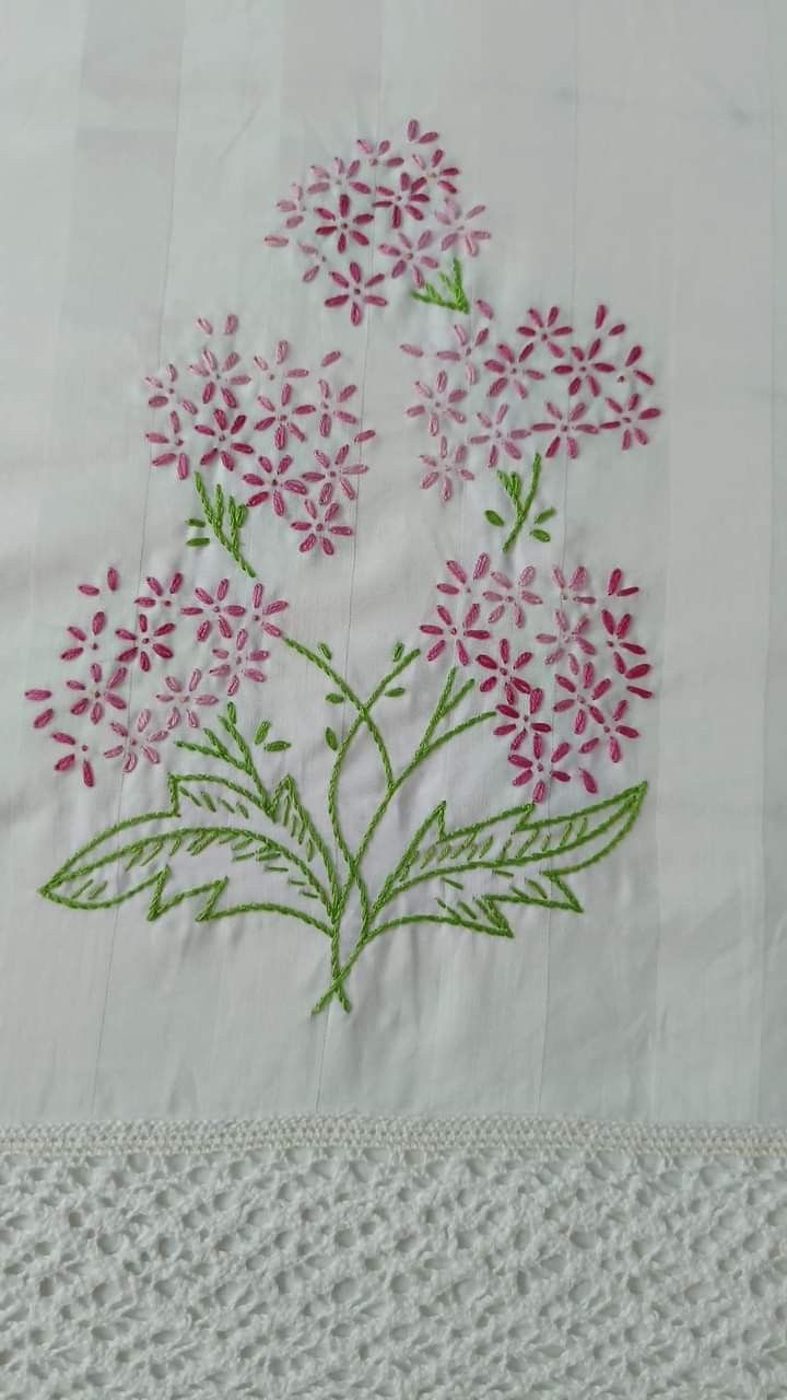 a white table cloth with pink flowers embroidered on the top and bottom, sitting on a lace doily