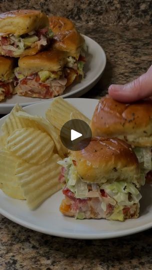 two plates with sandwiches and potato chips on the side, one has a bite taken out of it