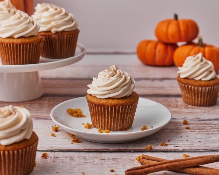 cupcakes with frosting and cinnamon sticks on a plate next to pumpkins