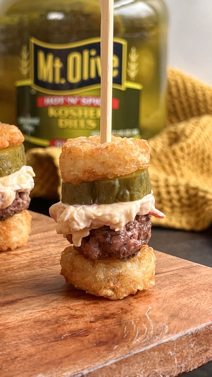 two hamburgers with pickles and mayonnaise on a cutting board