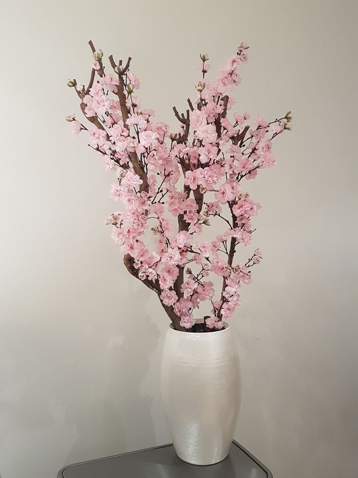 a white vase filled with pink flowers sitting on top of a black and silver table