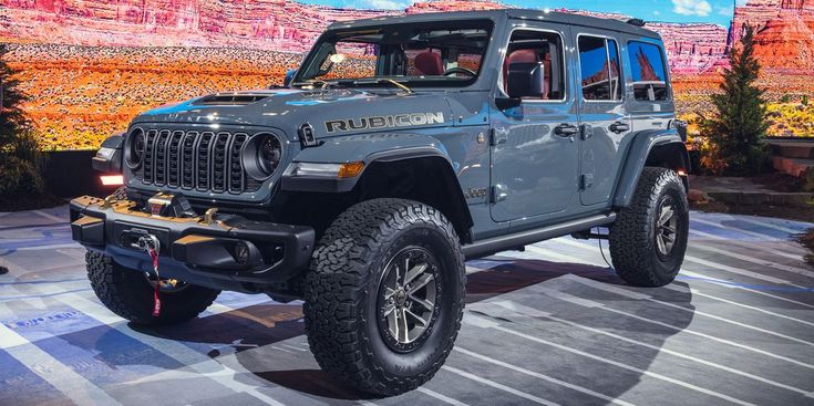 a blue jeep is on display at an auto show in front of a mountain backdrop