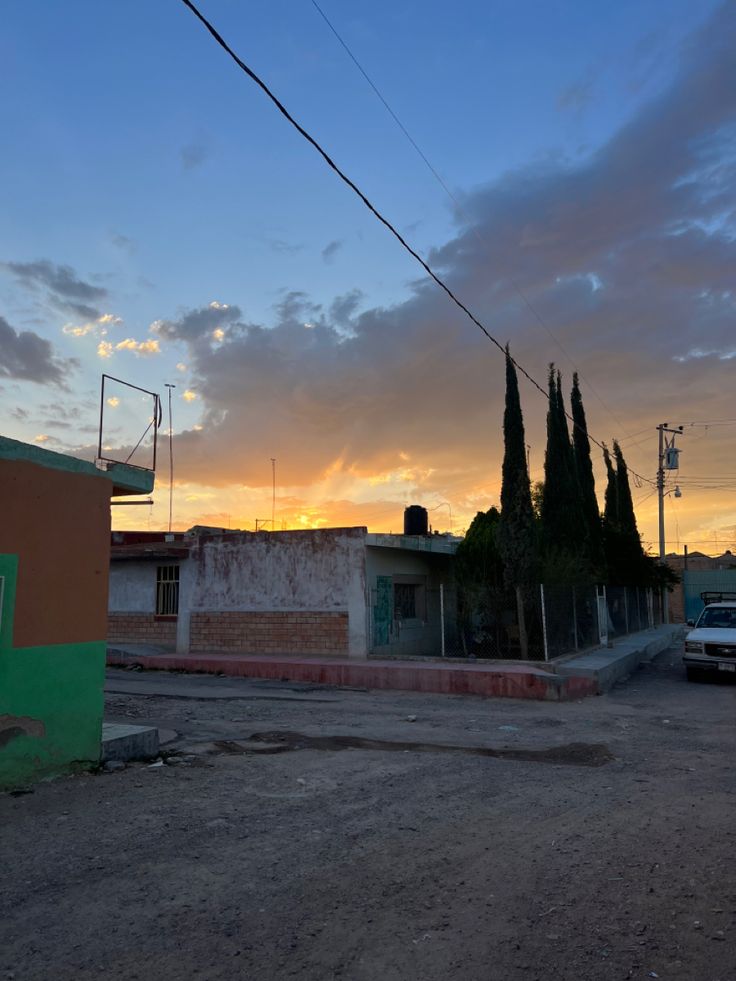 the sun is setting over an old building and some cars are parked on the street