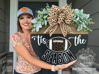 a woman holding up a football sign that says tis the season