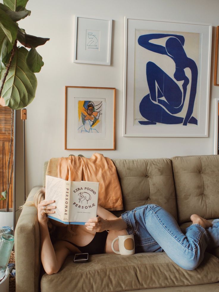 a woman sitting on top of a couch holding an open book in her hands and reading