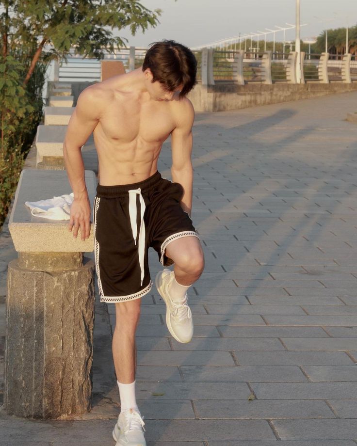 a shirtless man leaning on a tree stump with his leg up in the air