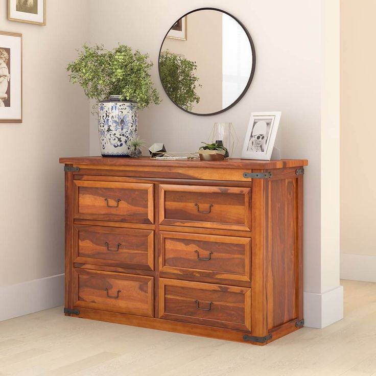 a wooden dresser sitting next to a wall with pictures on it and a round mirror above it